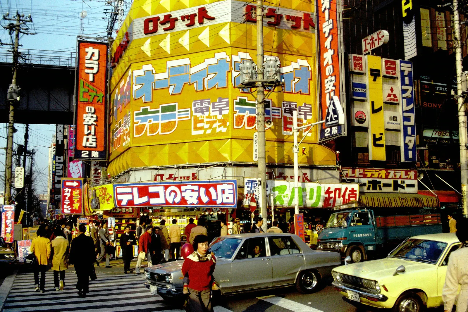 Akihabara shopfronts with yellow signs and vintage cars at a crossing