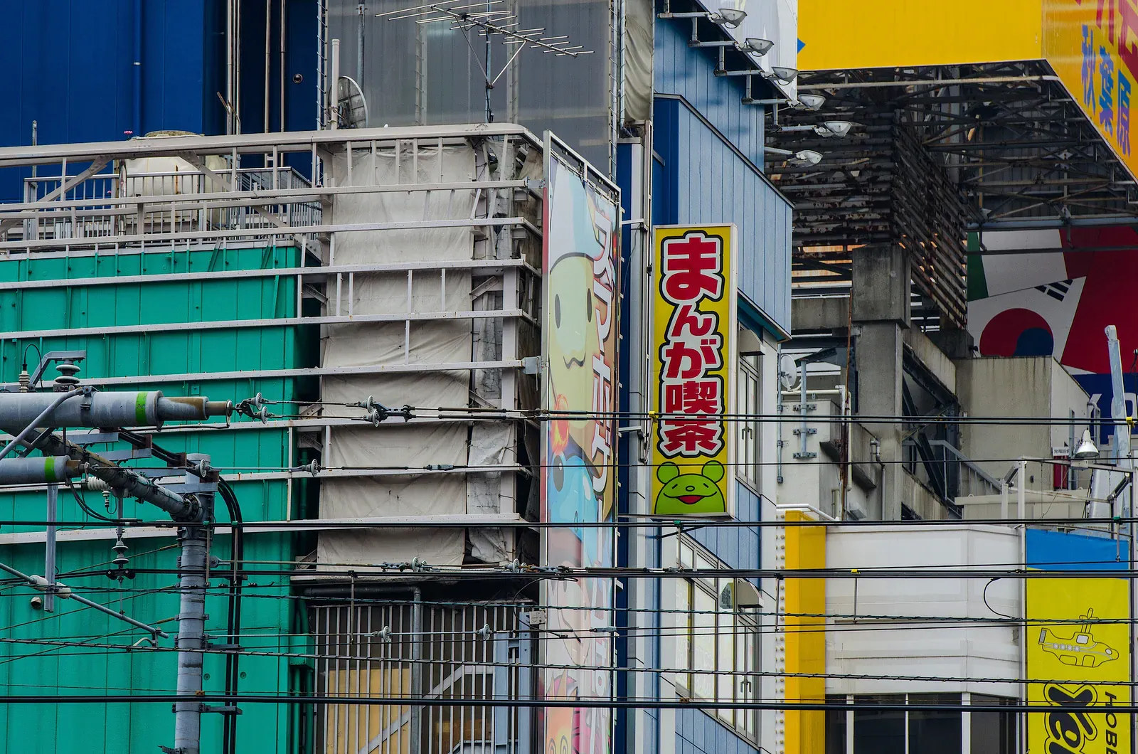 Rail-side building with a green wall and vertical manga cafe sign