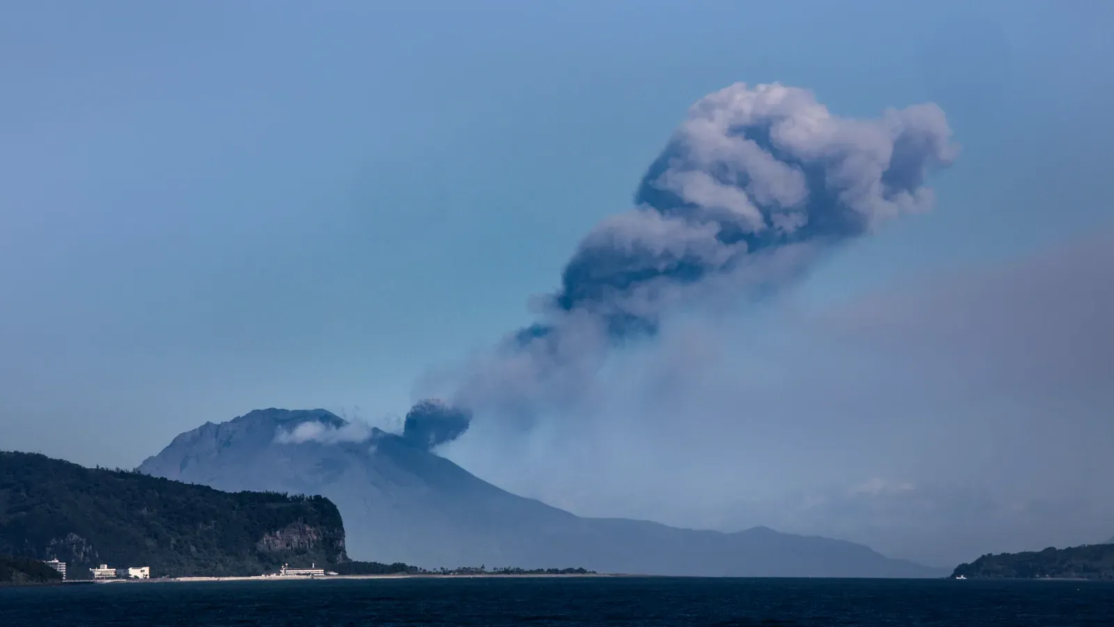 Grey ash plume rising from a volcano above a calm sea