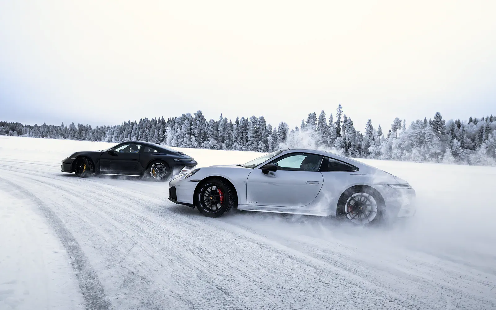Two Porsche sports cars sliding sideways across a snow-covered ice track