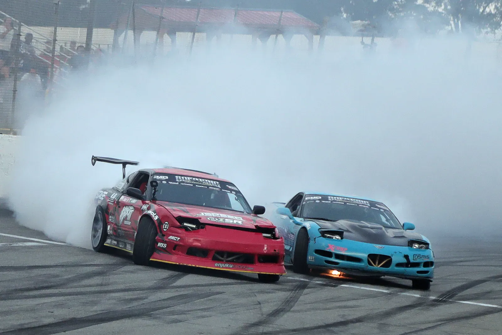 Red and blue drift cars sliding side by side in thick tyre smoke