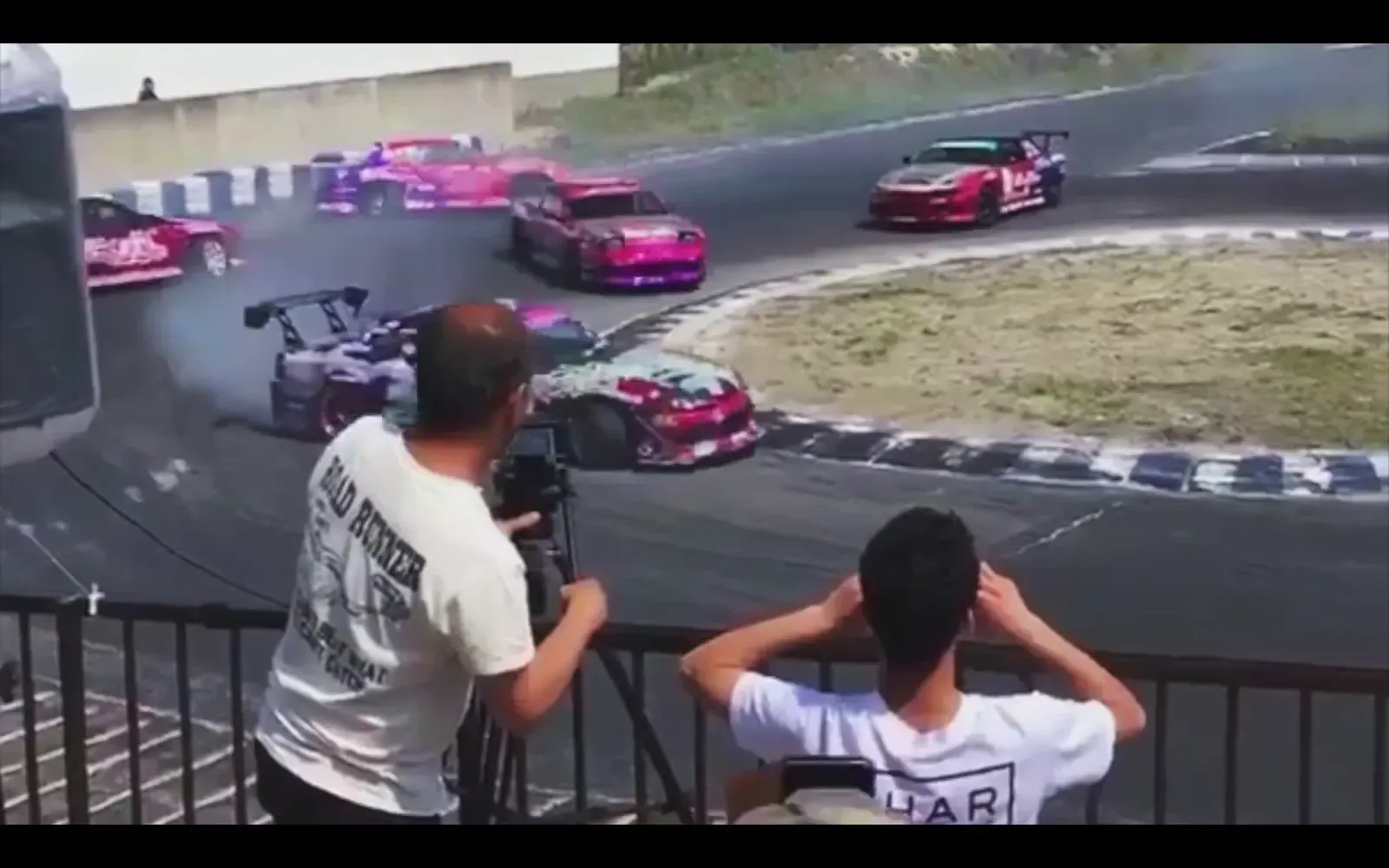 Spectators at a rail watching drift cars chase through a corner