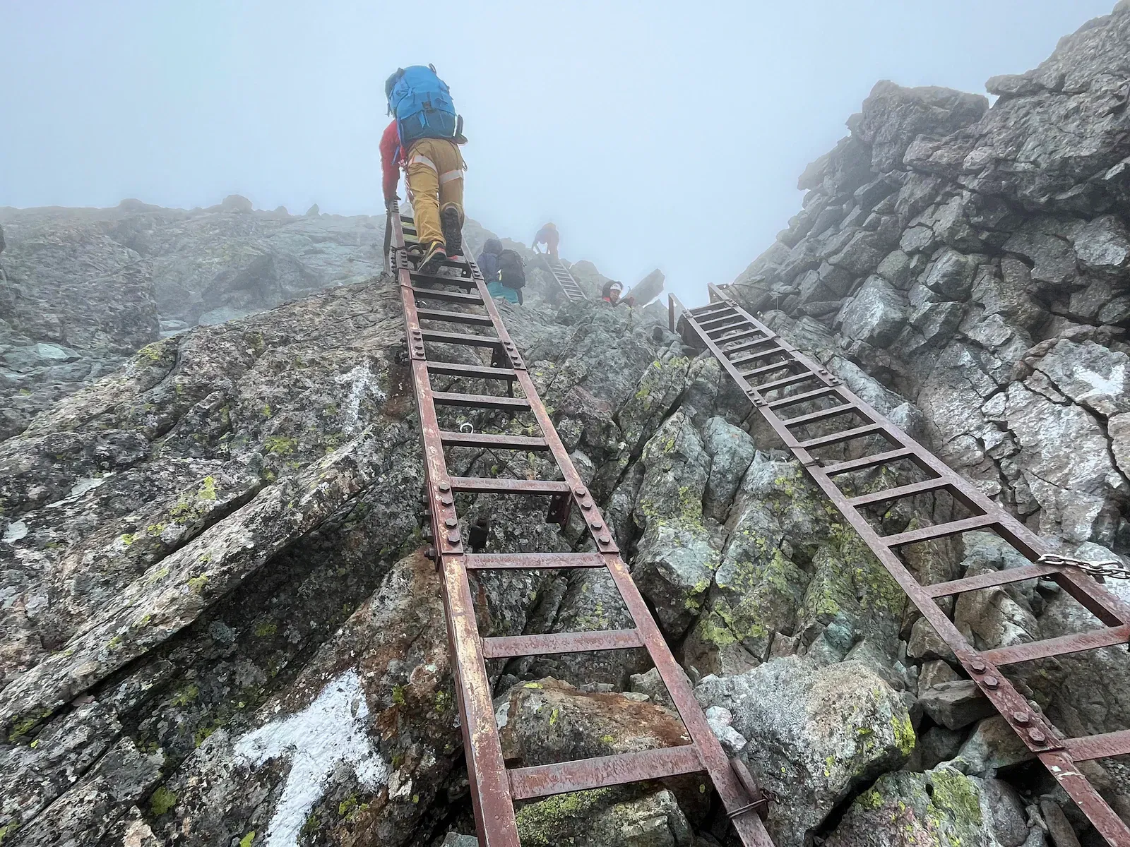 Hiker climbing iron ladders up a steep rocky Hotaka ridge in mist