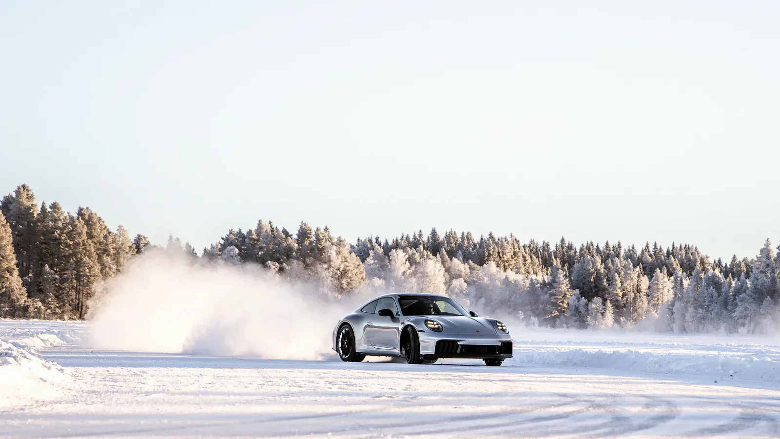 Silver sports car kicking up snow as it slides on a frozen track