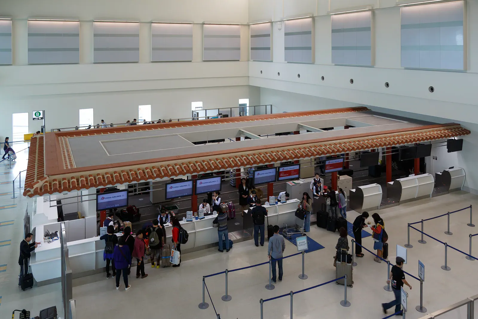 Travellers queuing at a Japanese airport check-in area under a tiled canopy