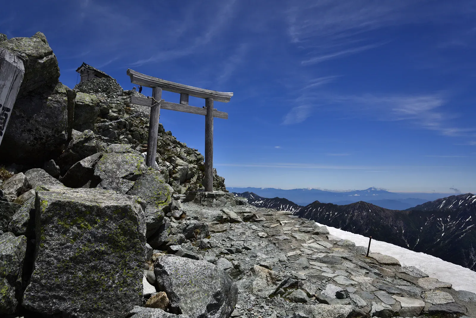 Wooden torii gate on a rocky summit path under a deep blue sky
