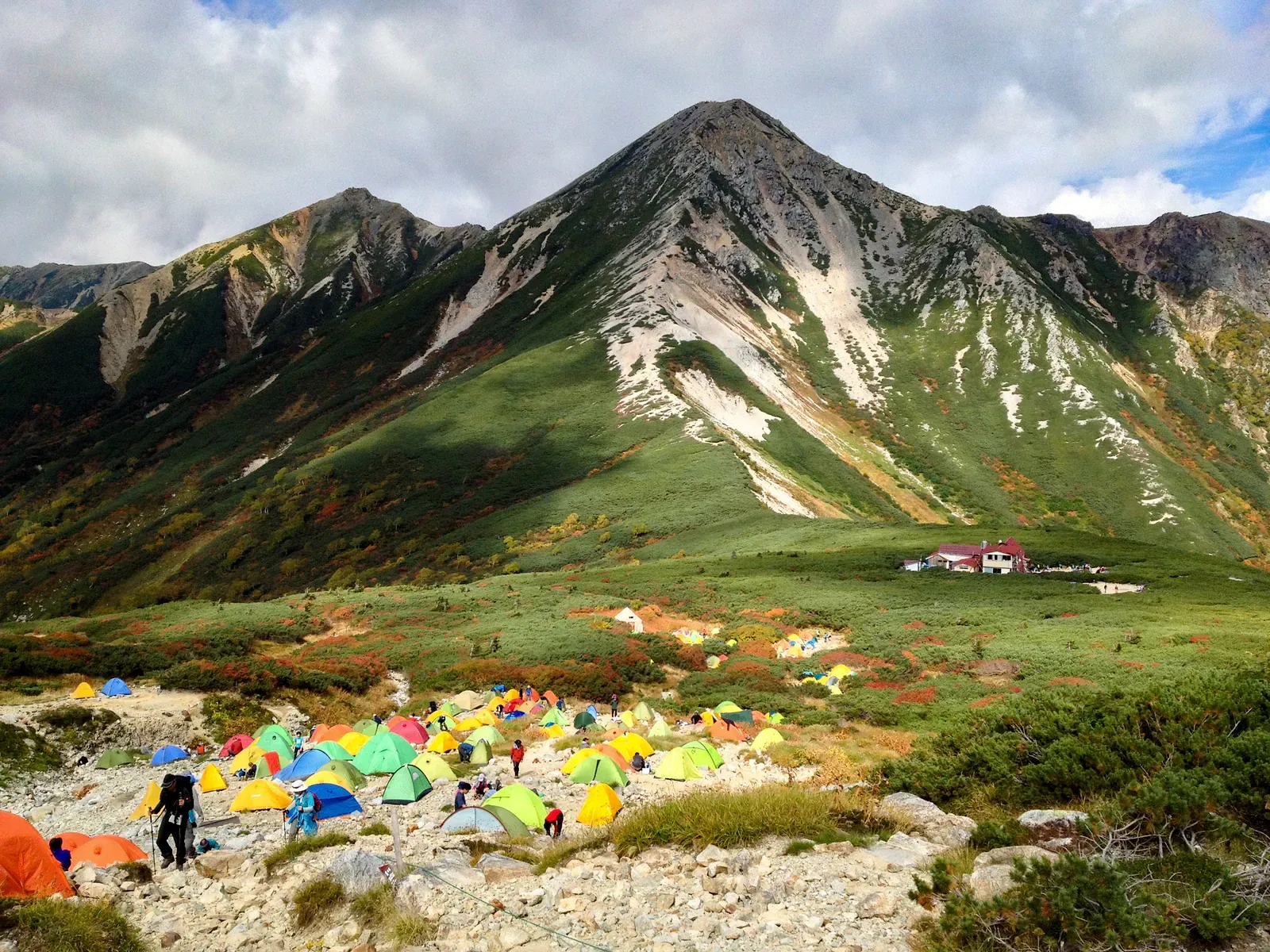 Colourful tents pitched below a sharp green Alps peak