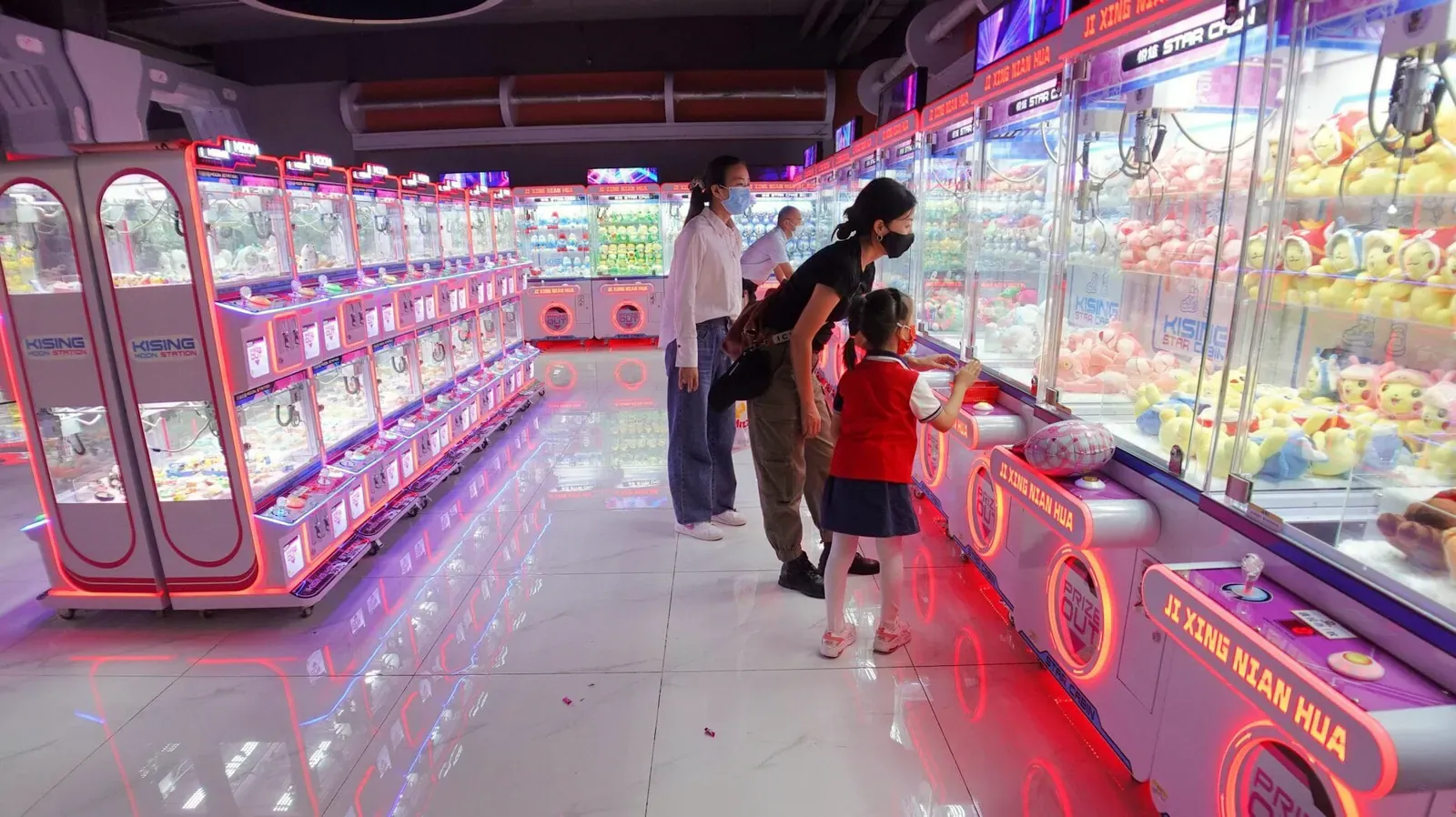 Family browsing a bright aisle of claw machines in a Japanese arcade