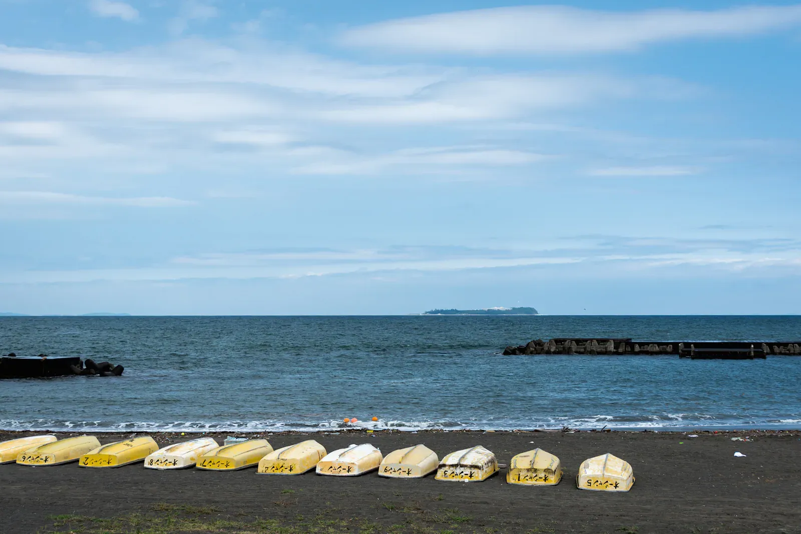 Row of yellow boats on a black sand beach beside a calm sea