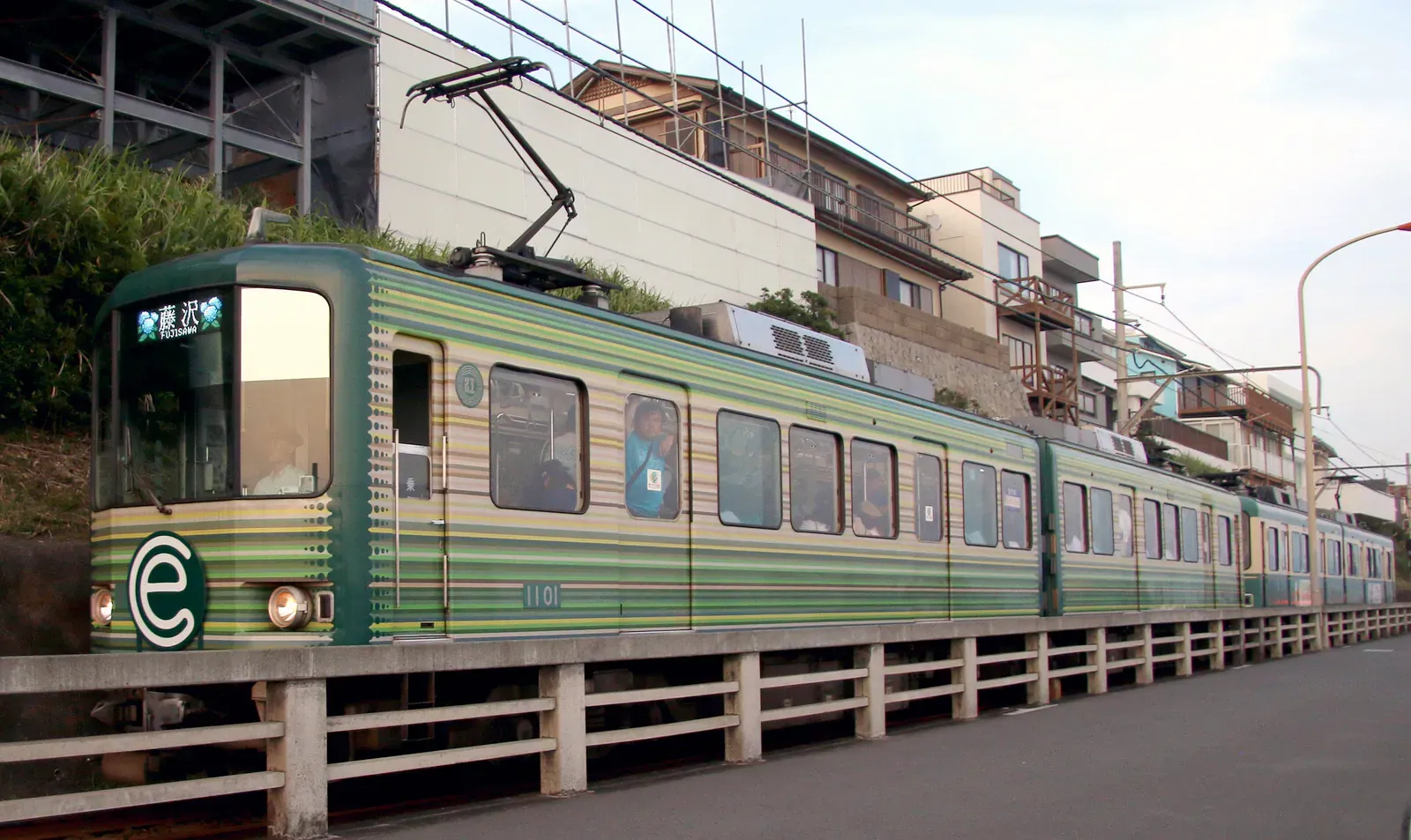 Green Enoden tram passing houses beside a low fence