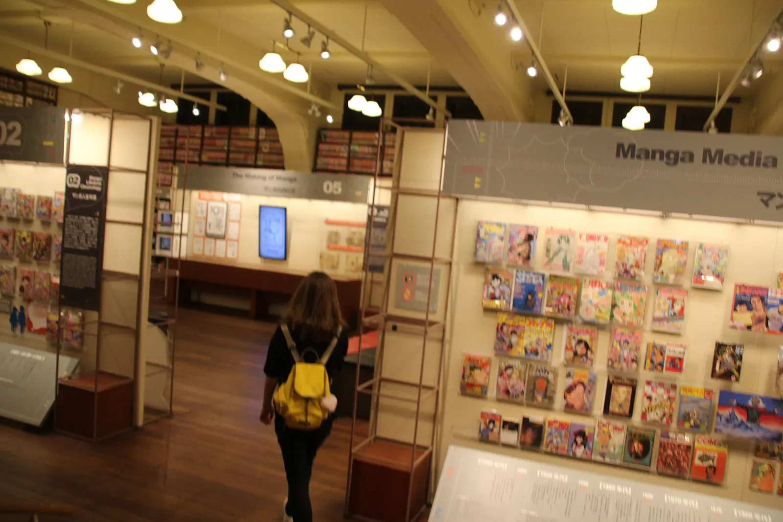 Visitor with yellow backpack in a manga gallery with wall of covers