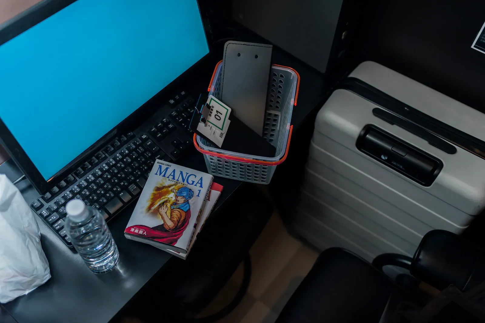 Laptop on a desk beside a manga magazine and a suitcase