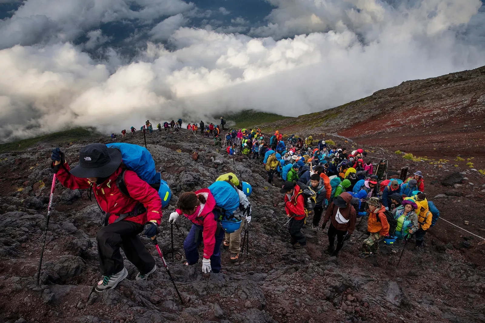 Long line of climbers in bright jackets filing up Fuji's volcanic slope