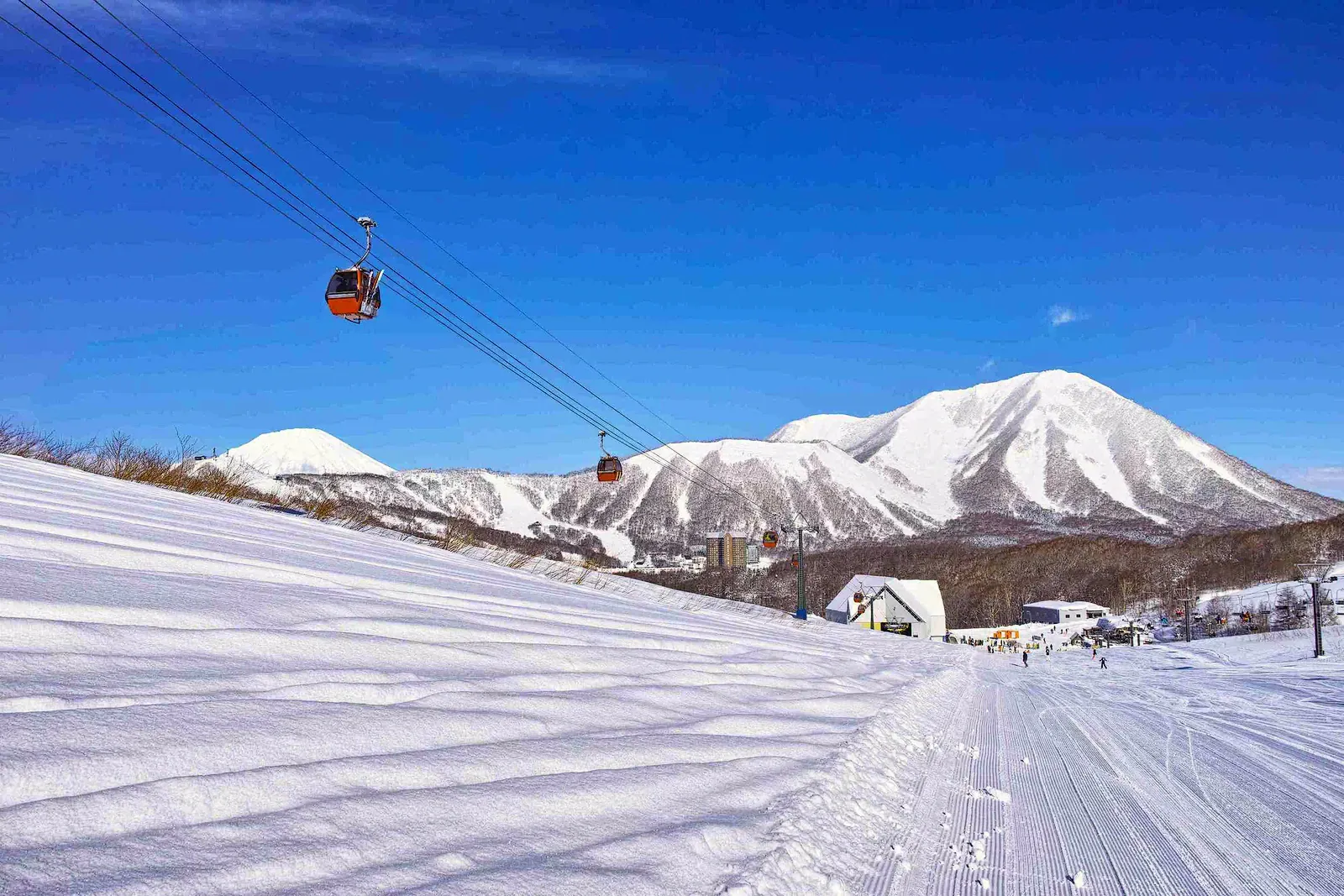 Gondola cabin above a freshly groomed run with snowy peaks behind