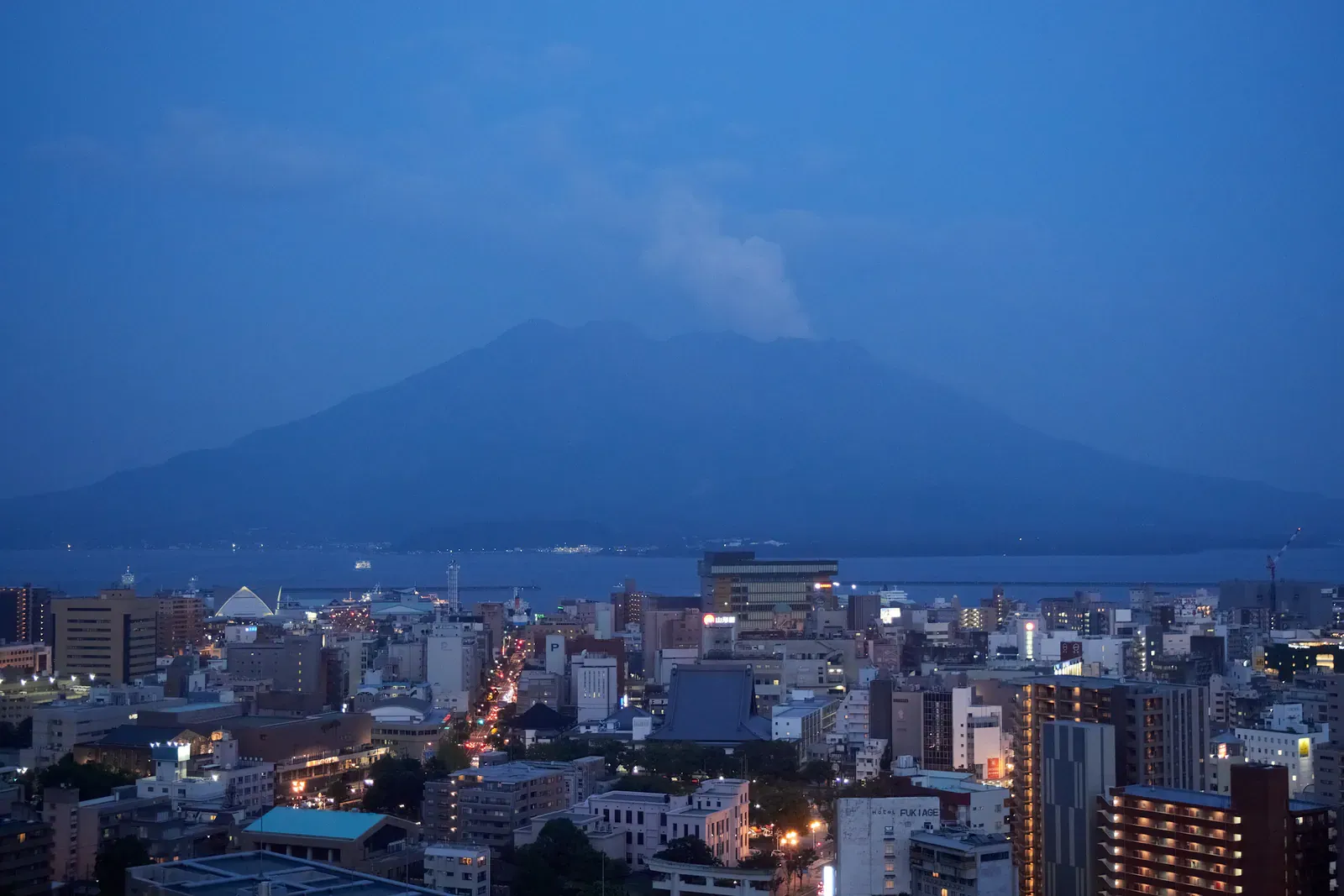Volcano silhouette above a city and bay at dusk