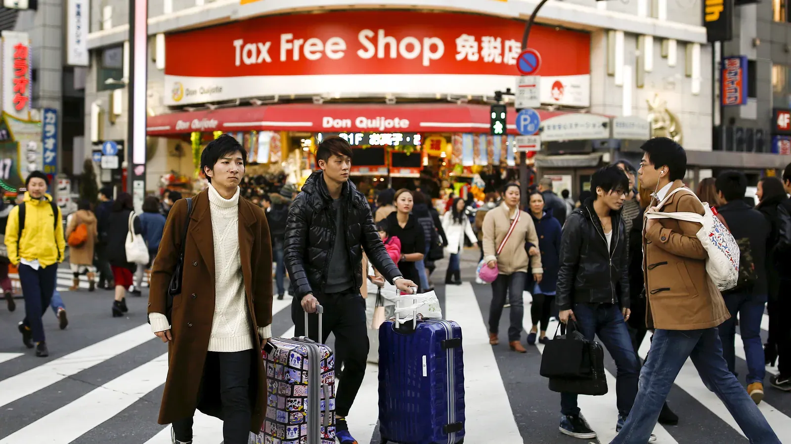 Shoppers with suitcases crossing in front of a red Tax Free Shop sign
