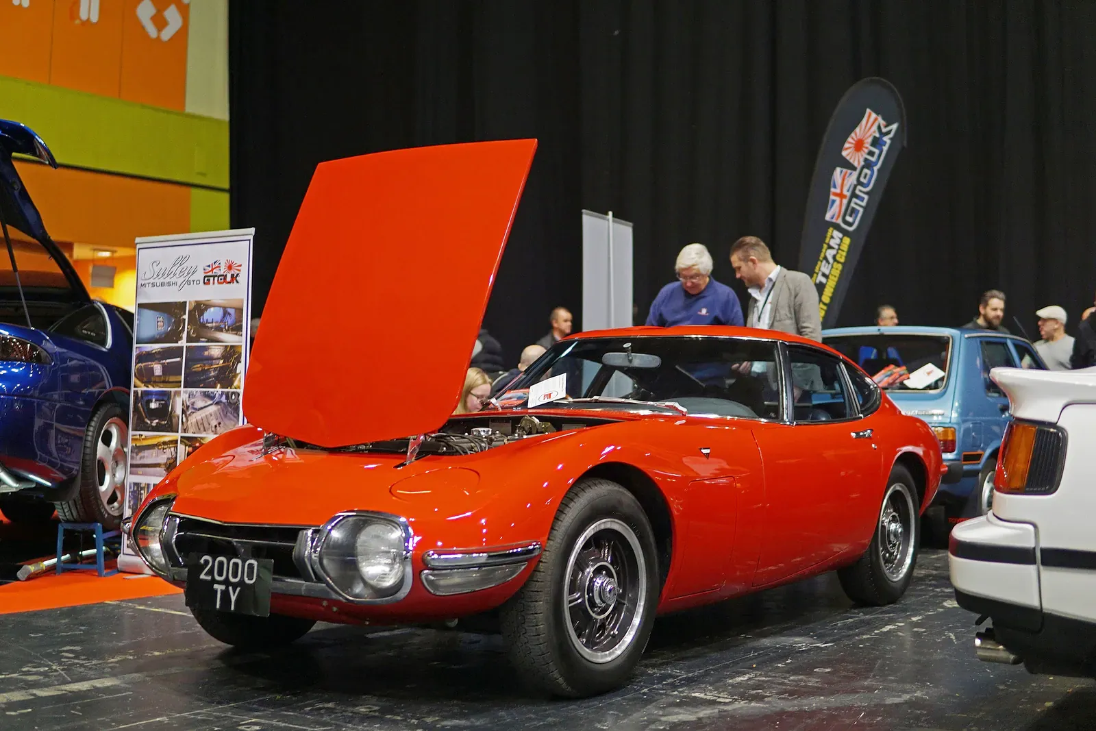 Orange Toyota 2000GT with its bonnet raised at a classic car show